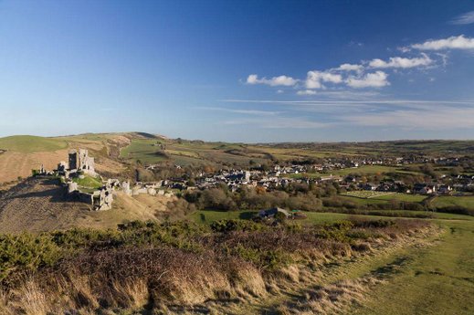 View of the ruins of Corfe Castle and the Village from the west hill behind the castle.  The east hill is to the left and the sea is in the far distance. 