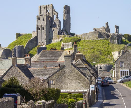 Must-Visit Places in Dorset: Your Guide to Unforgettable Experiences, the phootgraph is of the National Trust's Corfe Castle in the village of the same name. In the foreground are houses, shops and the main road through the village.